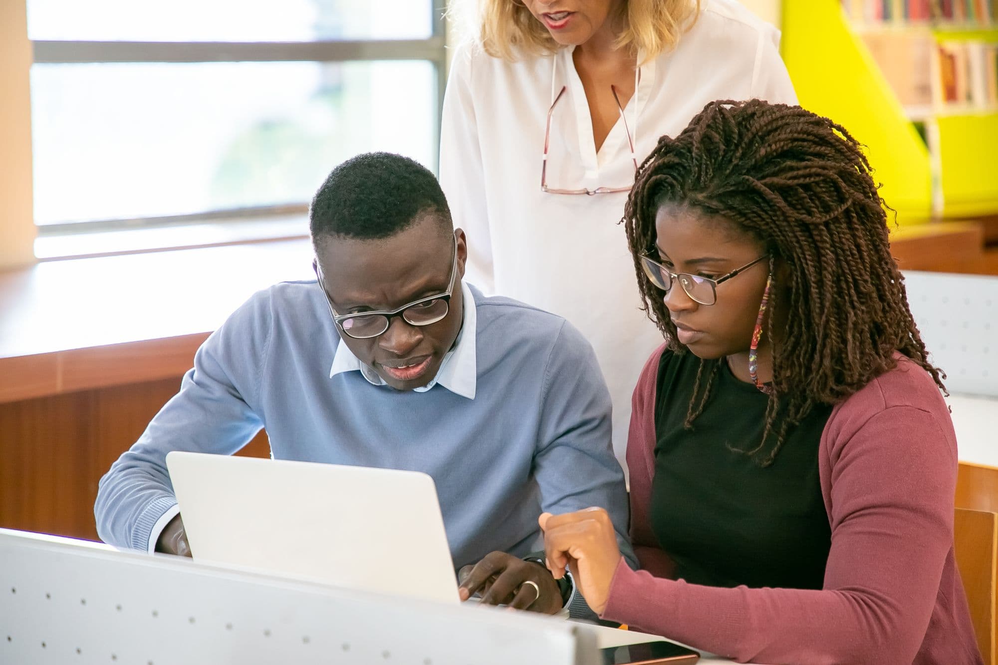 Two students and an instructor working together at a laptop in a library.